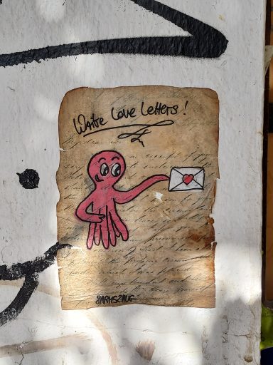 Streetart in Köln-Ehrenfeld, ein vergilbter Brief, auf den ein Krake gemalt ist, der einen Liebesbrief hält und sagt "Write Love Letters"